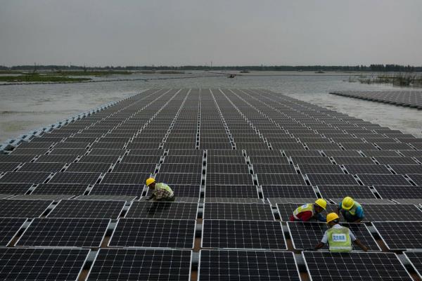 Trabajadores conectan los paneles solares a prueba de agua a boyas a la orilla del lago. New York Times