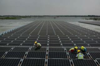Trabajadores conectan los paneles solares a prueba de agua a boyas a la orilla del lago. The New York Times